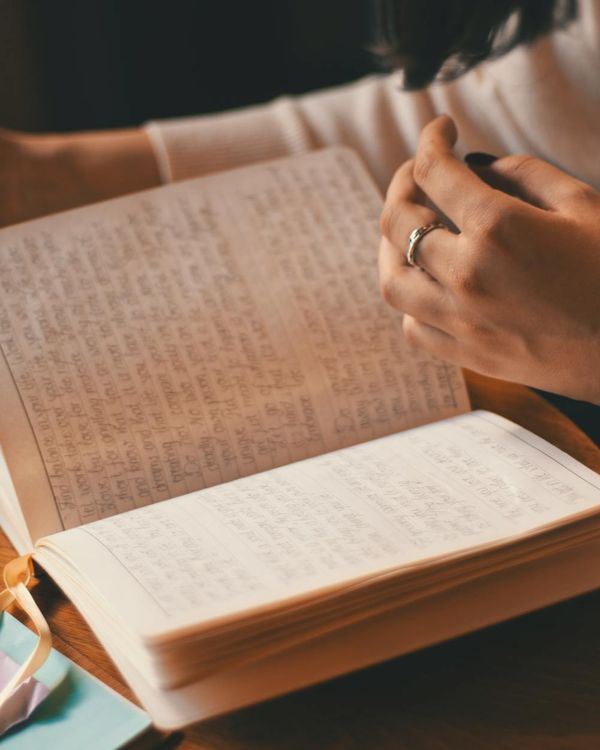 Person writing in a journal next to a cup of tea.